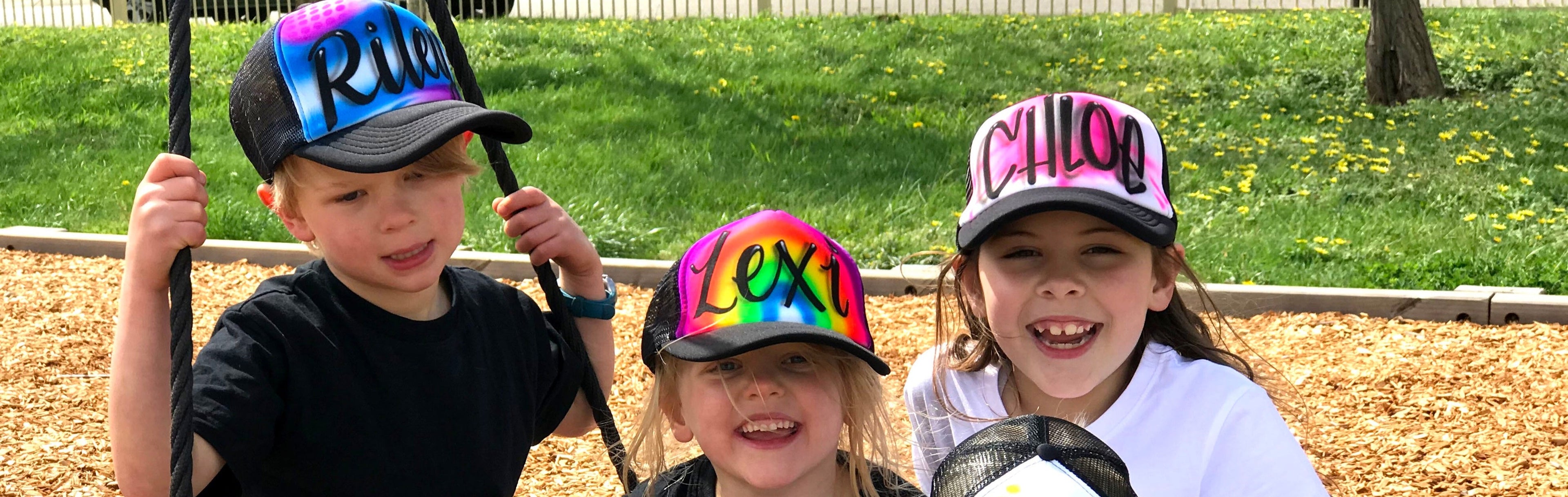 Three children on a playground with colourful airbrush personalised hats.