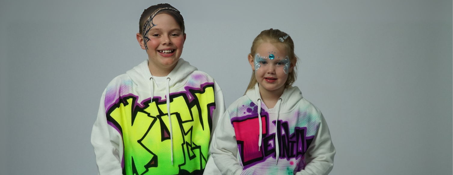 Two children wearing Airbrush colorful hoodies with graffiti-style text on a gray background