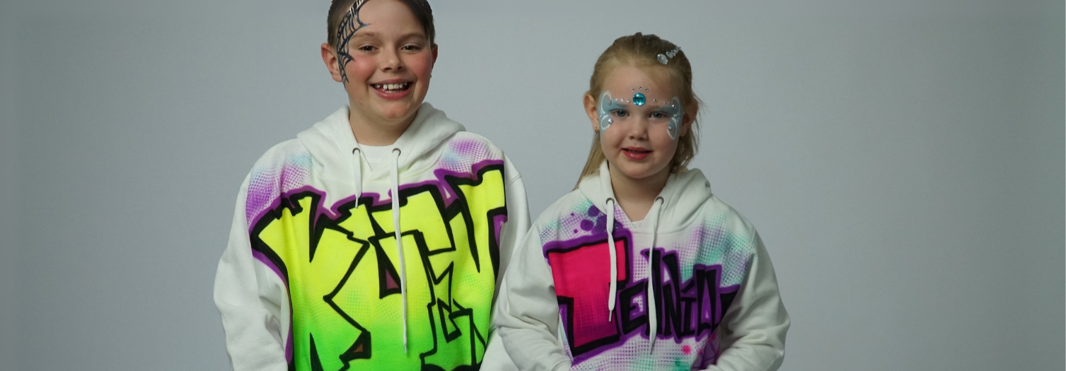 Two children wearing Airbrush colorful hoodies with graffiti-style text on a gray background