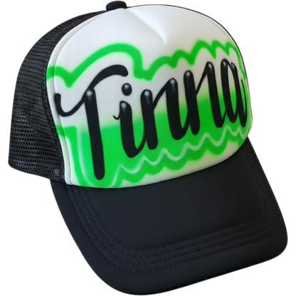 Black and white trucker cap with green design and black airbrush script text "Tinna" on a white background
