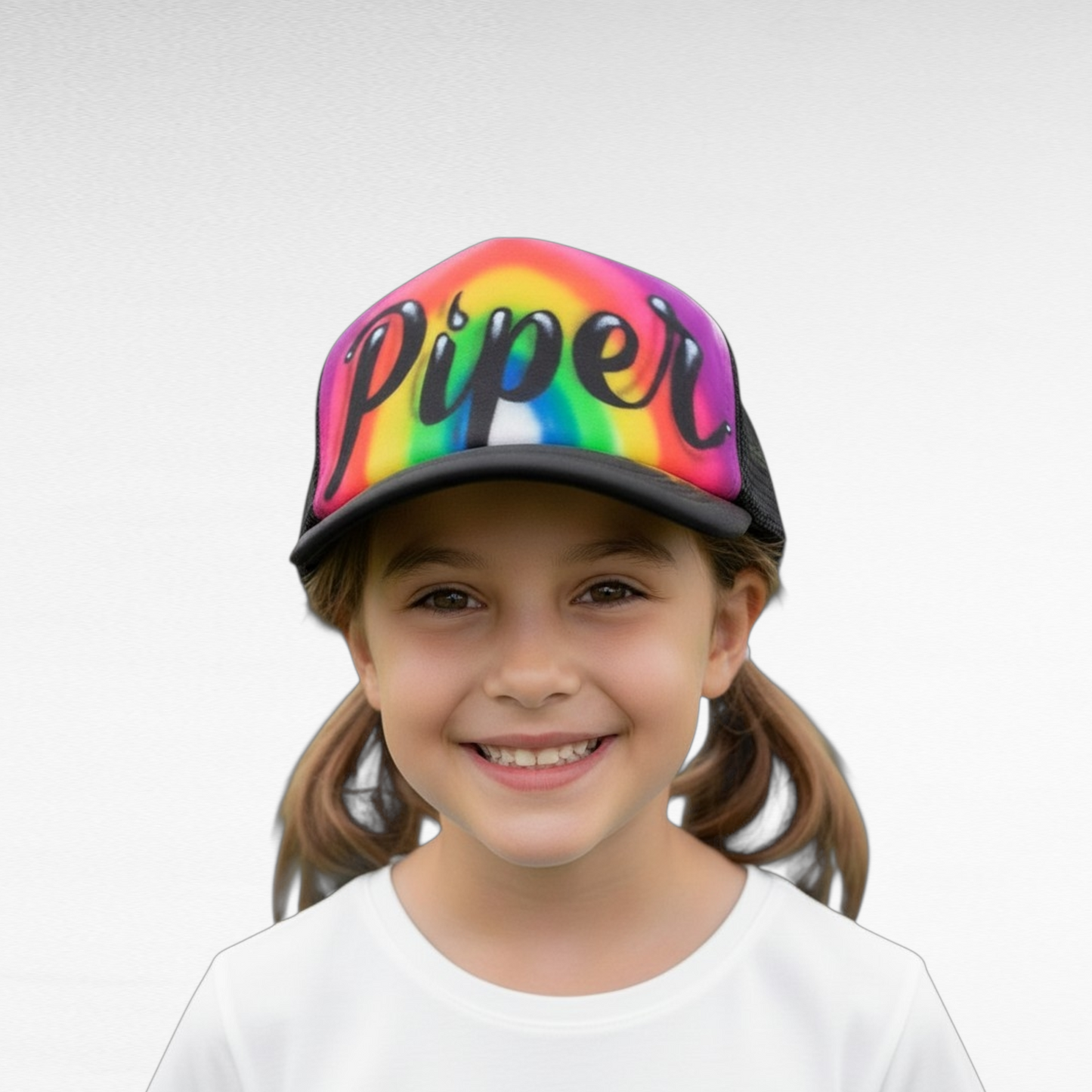 Child wearing a airbrush rainbow cap with 'Piper' on a white background