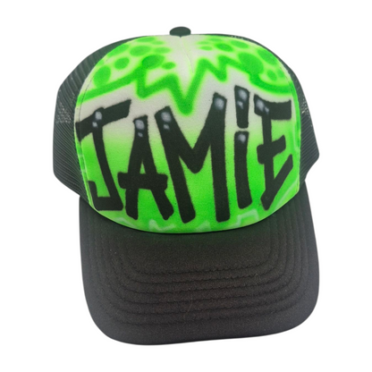 Black trucker cap with 'JAMIE' airbrushed with a green design on a white background
